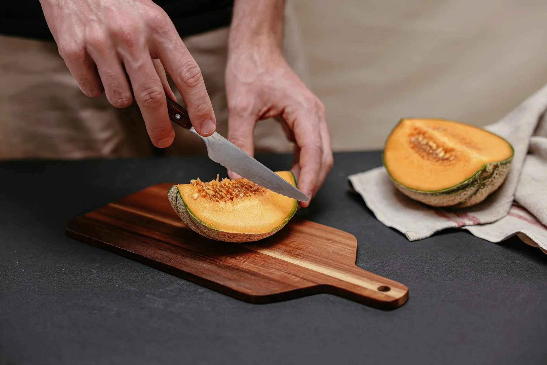 Hands slicing a melon on a chopping board